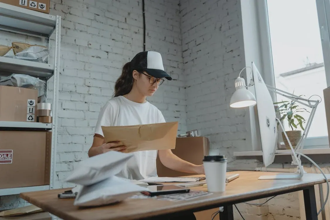 A small business owner holding a parcel at a desk. Boxes are stacked up behind them on a shelf